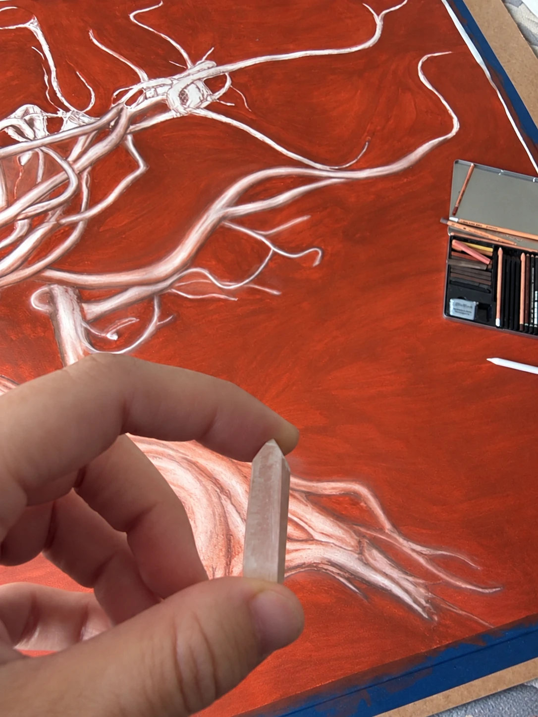 A hand holding a clear crystal in front of a red drawing of Sanguínea.