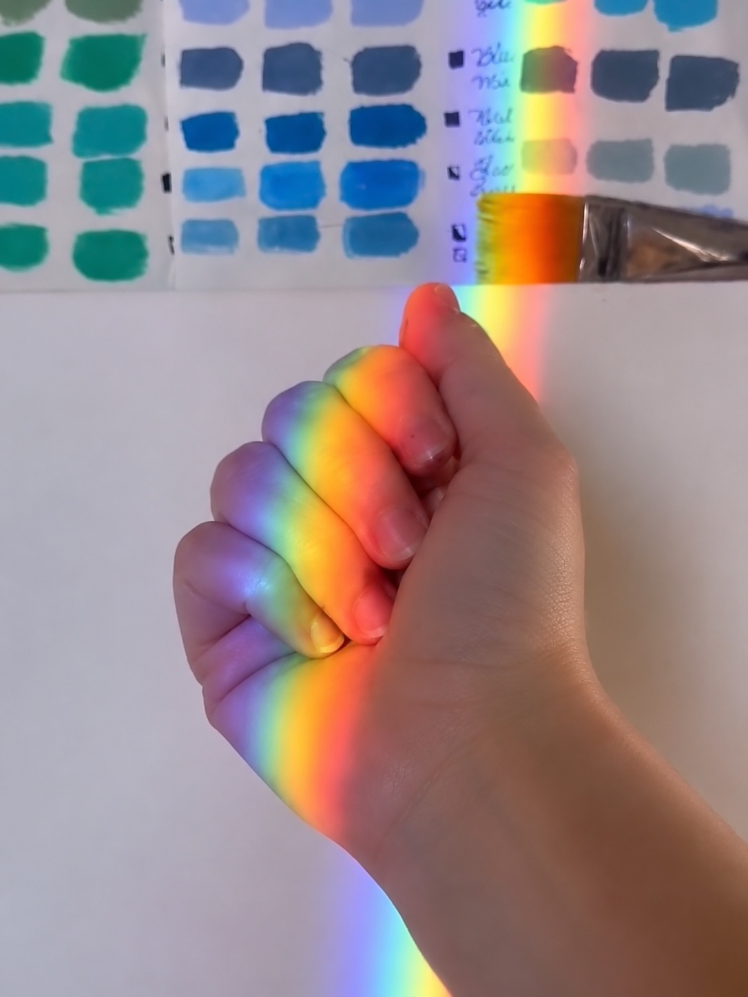 Rainbow light falling on a hand beside color samples.